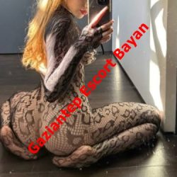 Woman in a black lace bodysuit kneels on a dark floor and takes a mirror selfie; red diagonal text reads 'Gaziantep Escort Bayan'.