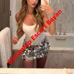 Mirror selfie of a woman in a white tank top and silver sequin mini skirt in a bathroom, with red diagonal text 'Gaziantep Escort Bayan' across her torso.