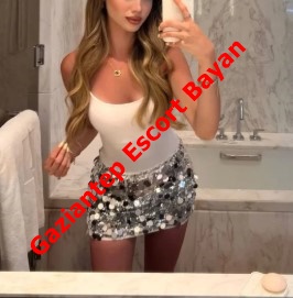 Mirror selfie of a woman in a white tank top and silver sequin mini skirt in a bathroom, with red diagonal text 'Gaziantep Escort Bayan' across her torso. Mirror selfie of a woman in a white tank top and silver sequin mini skirt in a bathroom, with red diagonal text 'Gaziantep Escort Bayan' across her torso.