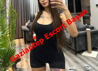 Woman in a black sleeveless outfit taking a mirror selfie in a modern living room; bold red overlay reads Gaziantep Escort Bayan.