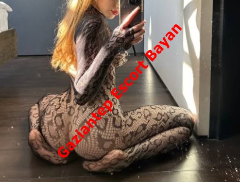 Woman in a black lace bodysuit kneels on a dark floor and takes a mirror selfie; red diagonal text reads 'Gaziantep Escort Bayan'.