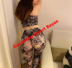 Woman in black floral lace lingerie standing with her back to the camera in a living room; red diagonal watermark reads 'Gaziantep Escort Bayan' across the image, indicating an escort advertisement.