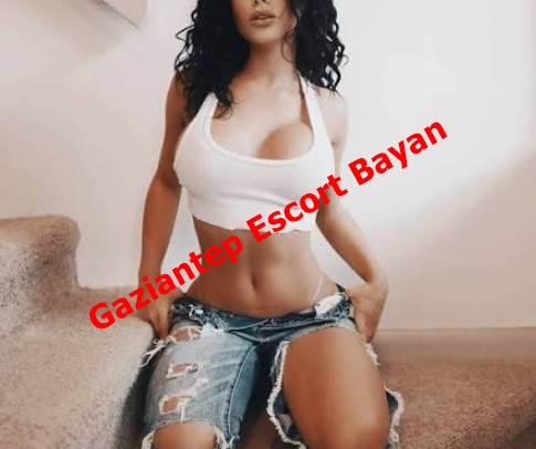 Woman in a white crop top and ripped denim shorts posing on stairs, with a red diagonal watermark reading 'Gaziantep Escort Bayan'.